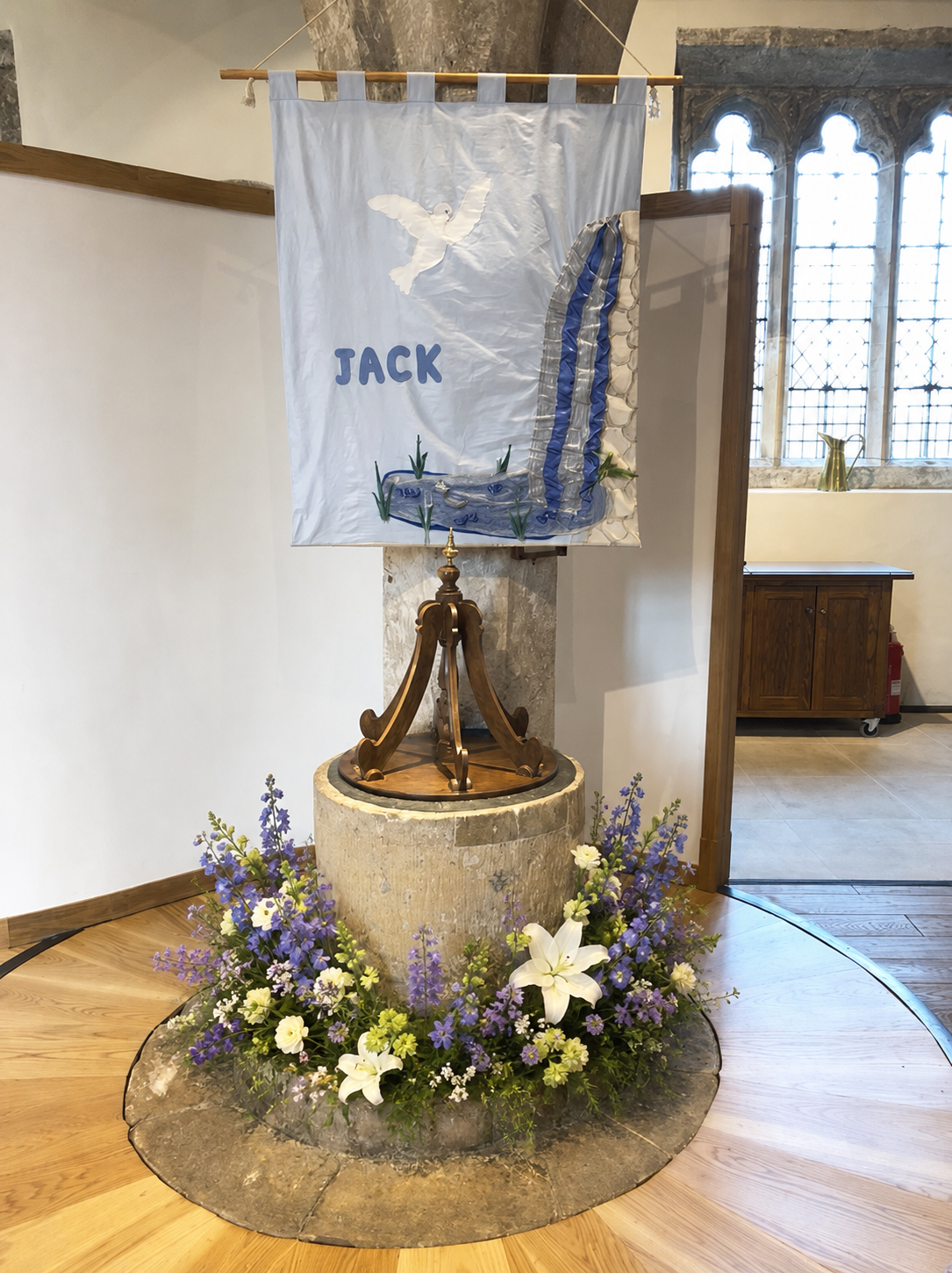 A decorated baptism font with flowers and a banner reading Jack
